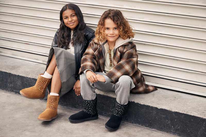 Two kids sat on a curb in stylish fits wearing Koolaburra kids boots.