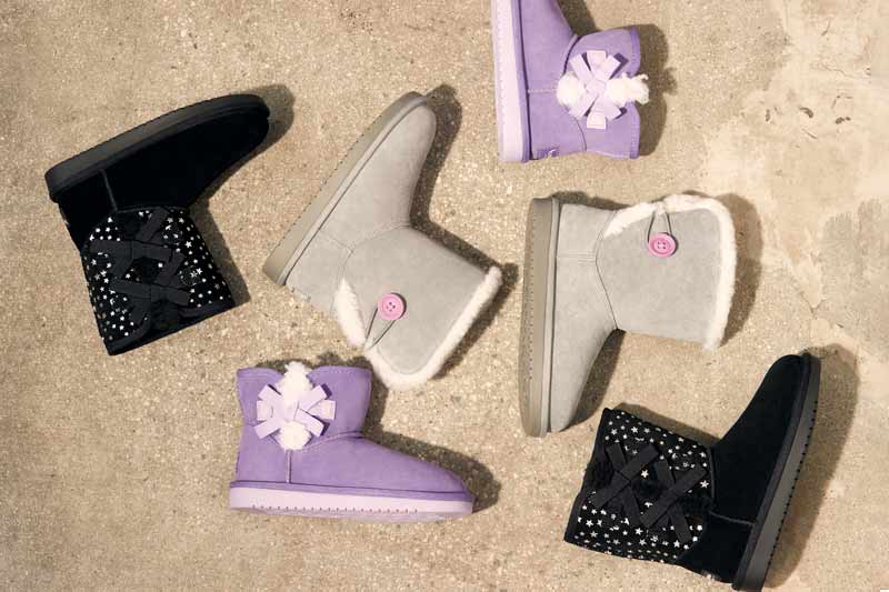 A selection of Koolaburra kids boots arranged in an aesthetically pleasing way on a concrete backdrop.
