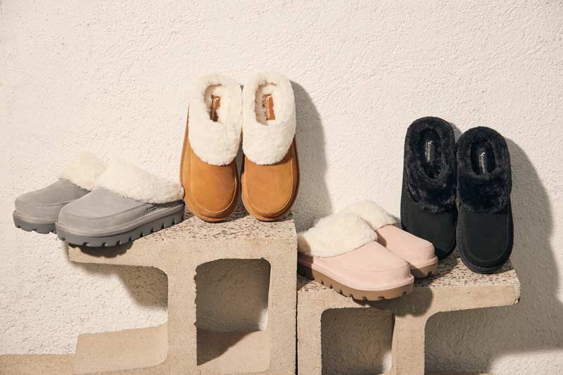 A selection of Koolaburra shoes and slippers arranged in an aesthetically pleasing way on a concrete backdrop.
